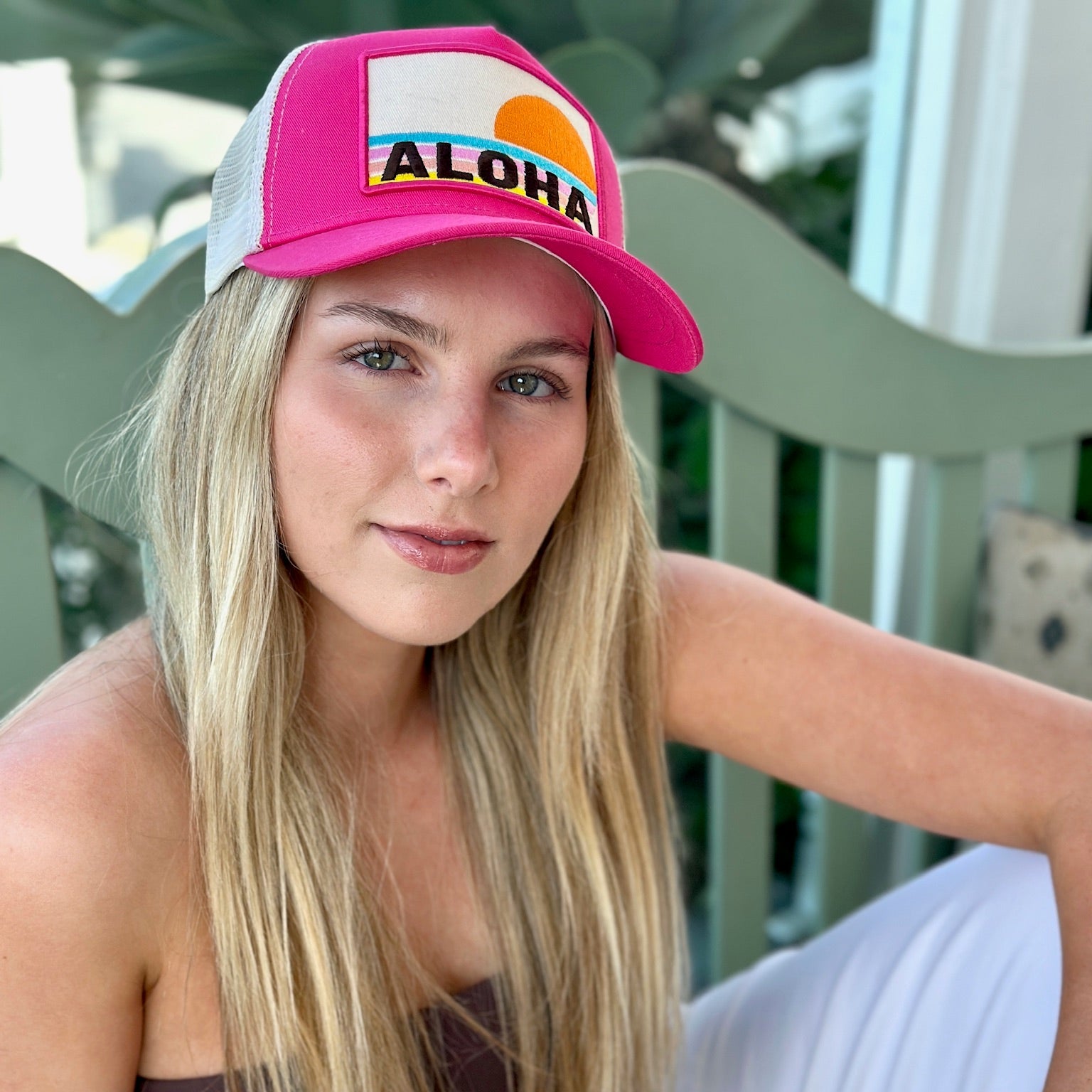 Pink Aloha trucker hat with embroidered sun and stripes worn by woman