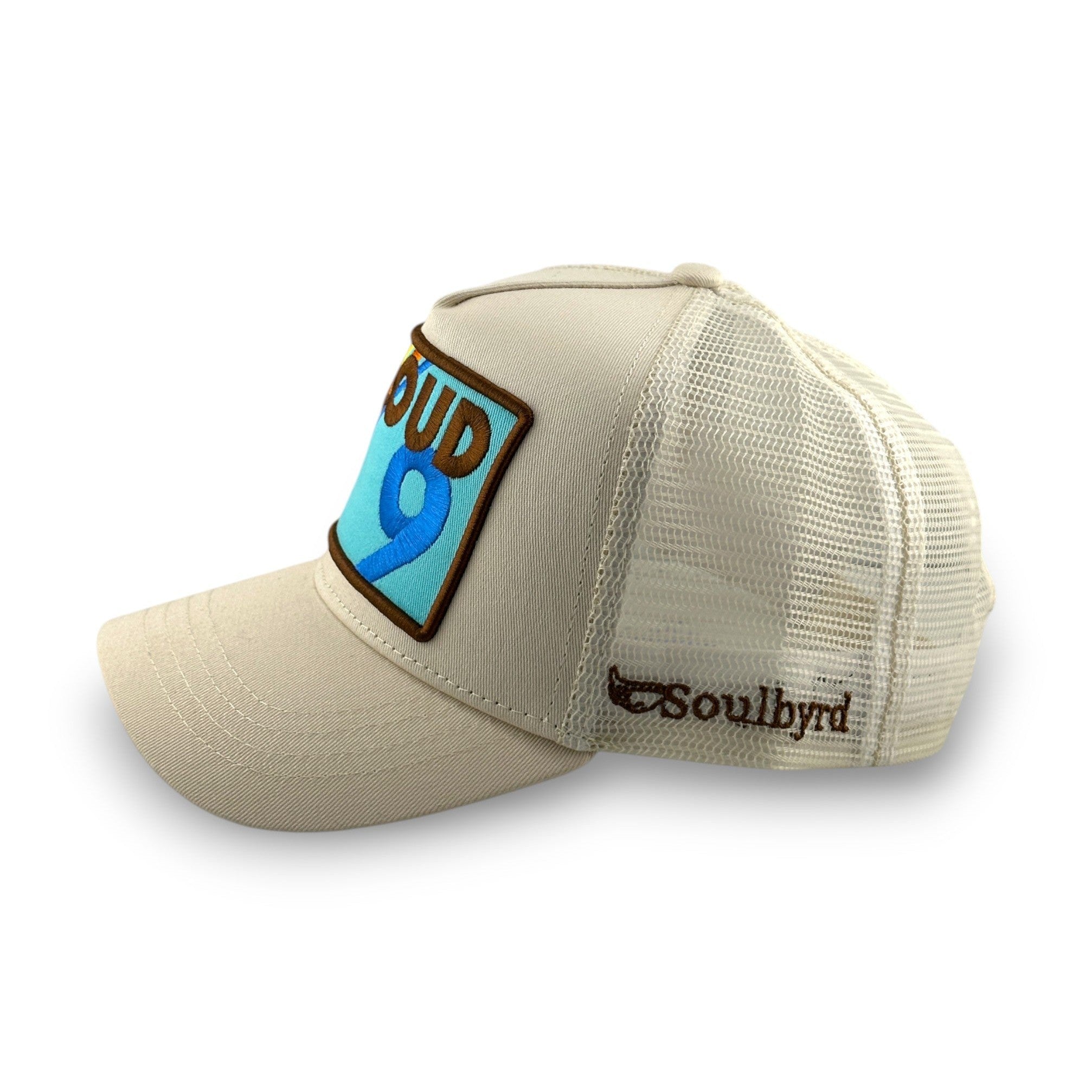 Side view of cream Soulbyrd trucker hat showing mesh back and embroidered brand logo