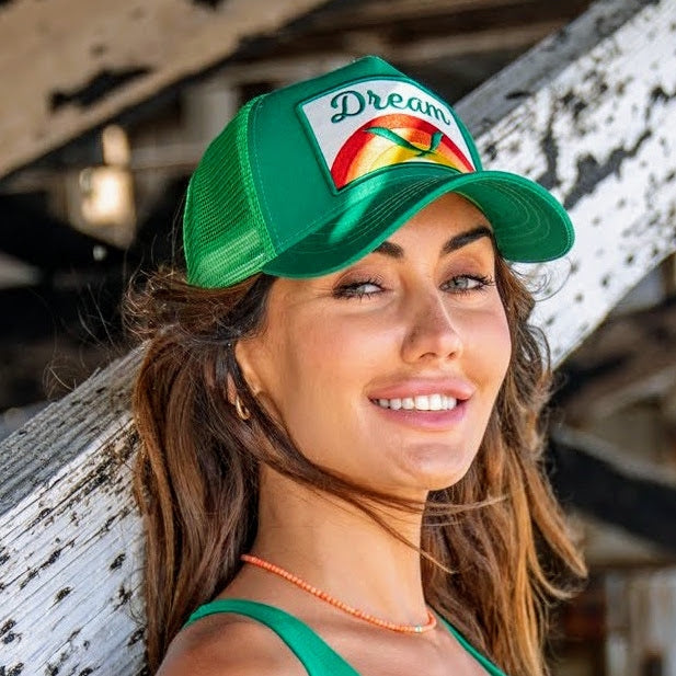 Woman wearing green adjustable trucker hat with dream motif in outdoor setting