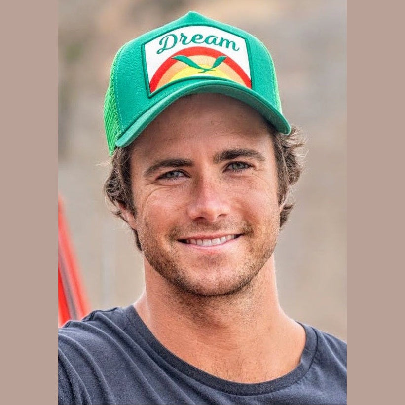 Man modeling green Dream Trucker hat with front rainbow bird patch