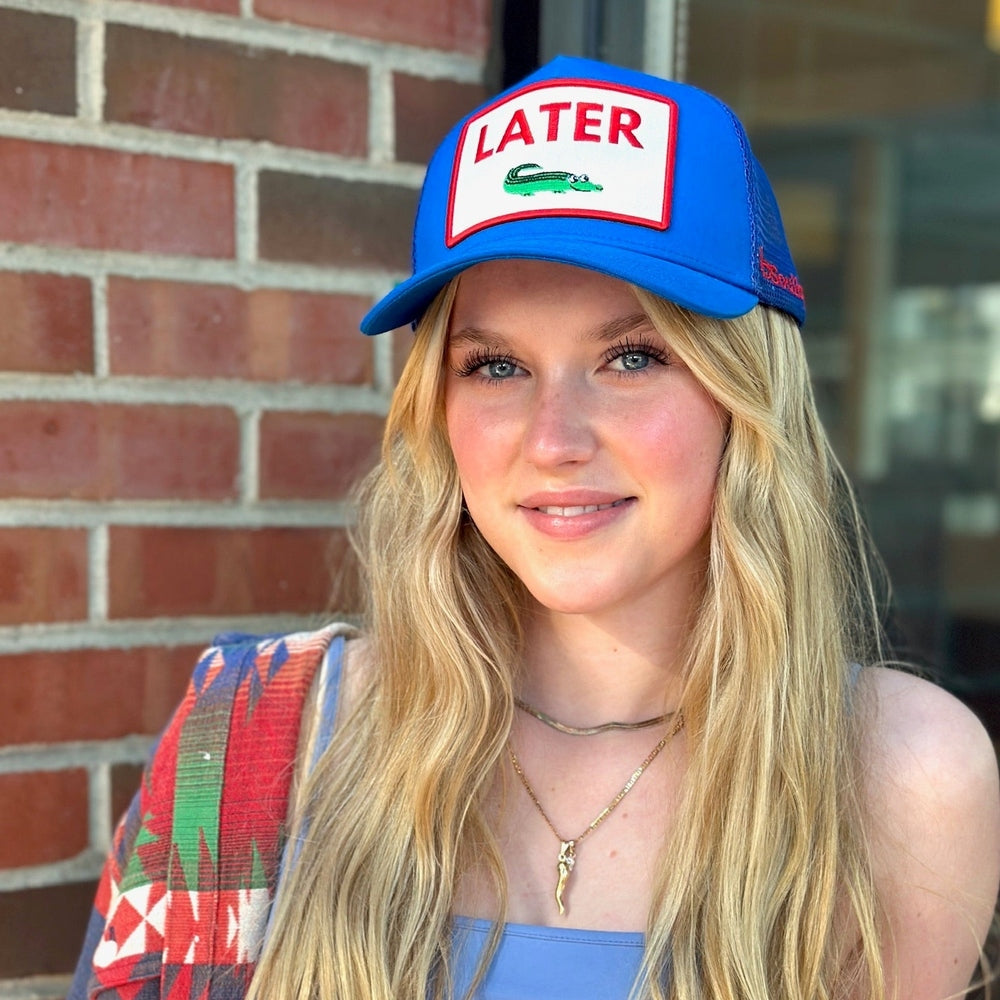 Woman wearing royal blue 5-panel trucker hat with green alligator graphic
