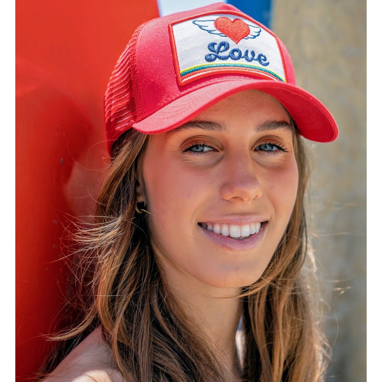 Woman wearing red Soulbyrd Love Wings trucker hat with heart and rainbow patch