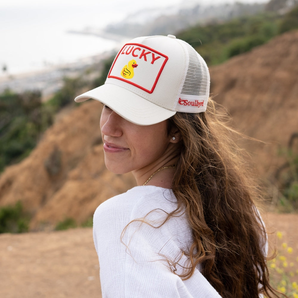 Woman wearing cream Soulbyrd trucker hat featuring red embroidered brand text on mesh side