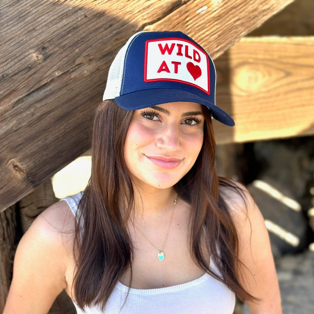 Woman wearing navy blue Wild at Heart trucker hat with red heart patch outdoors