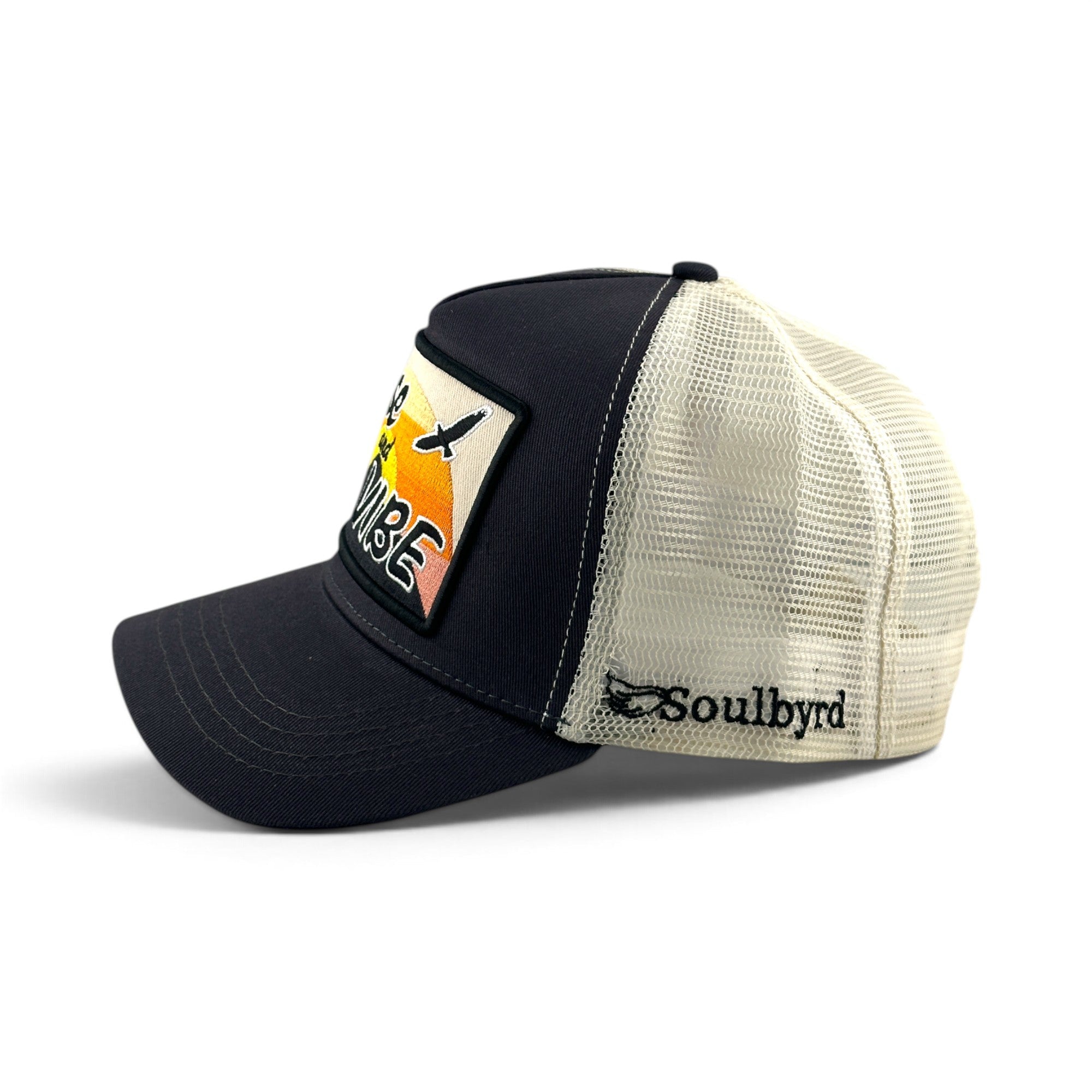 Soulbyrd Wholesale charcoal and white mesh trucker hat with Rise & Vibe sunset graphic patch and snapback closure.